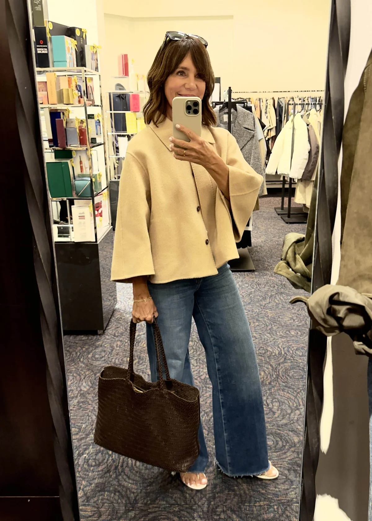 Stylish woman trying on a cream jacket and jeans at Nordstrom