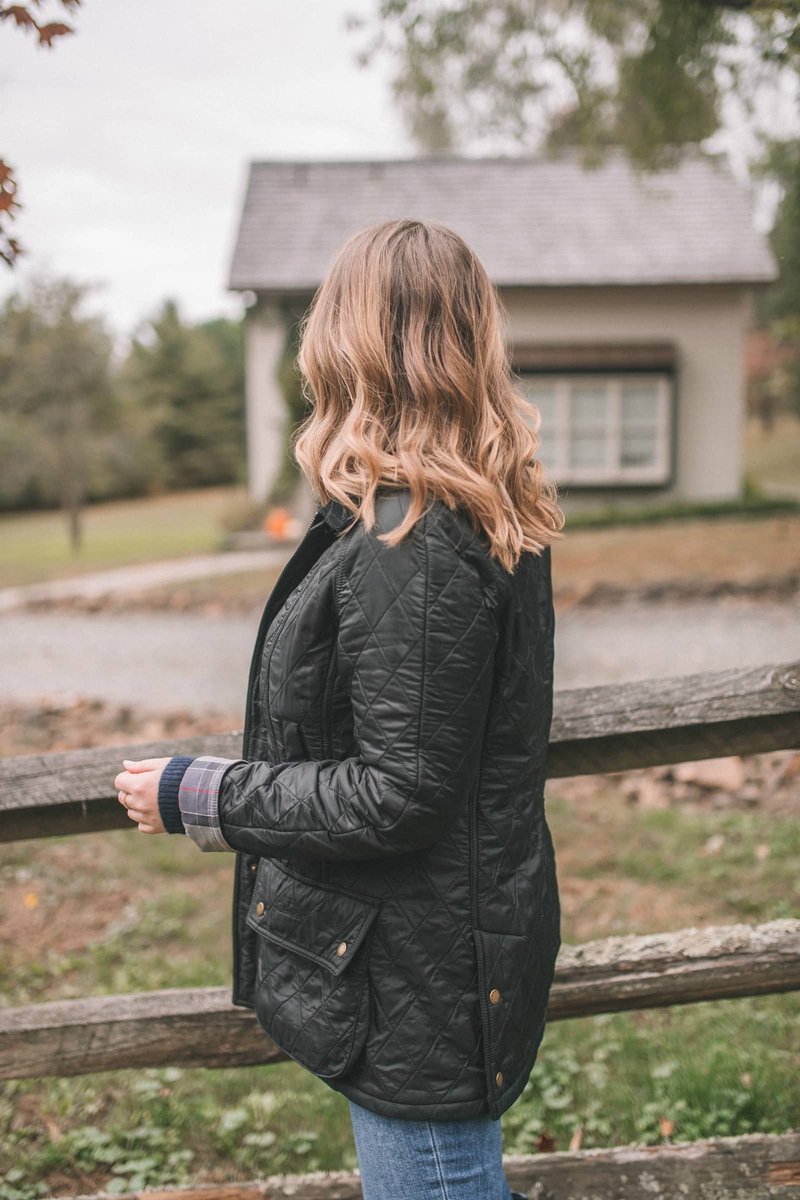 Woman in black quilted jacket standing by wooden fence outdoors