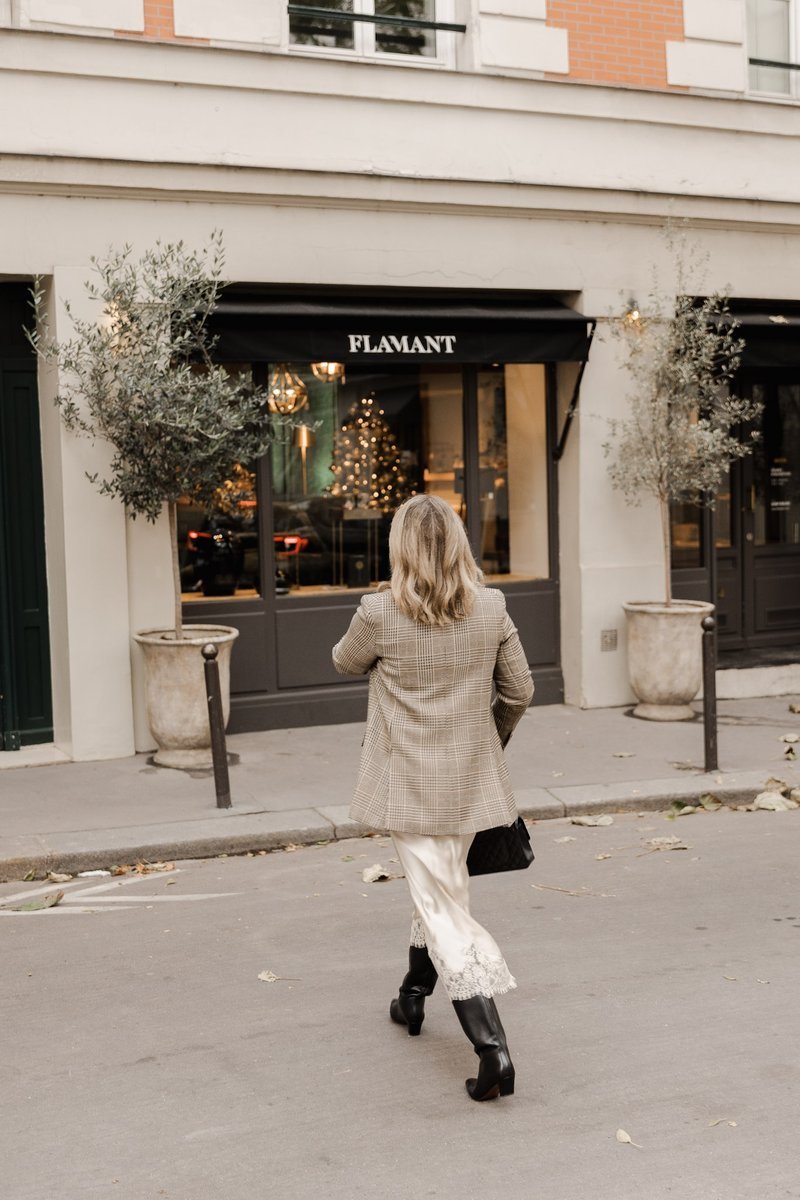 Woman in plaid blazer and boots walking past storefront
